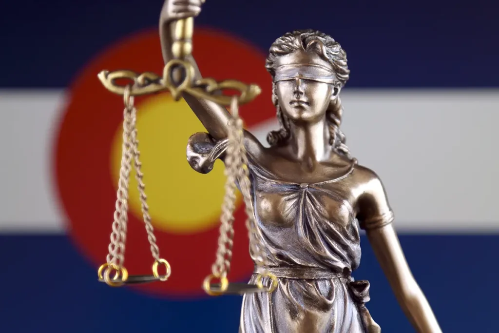 A bronze law and order statue in front of the Colorado state flag